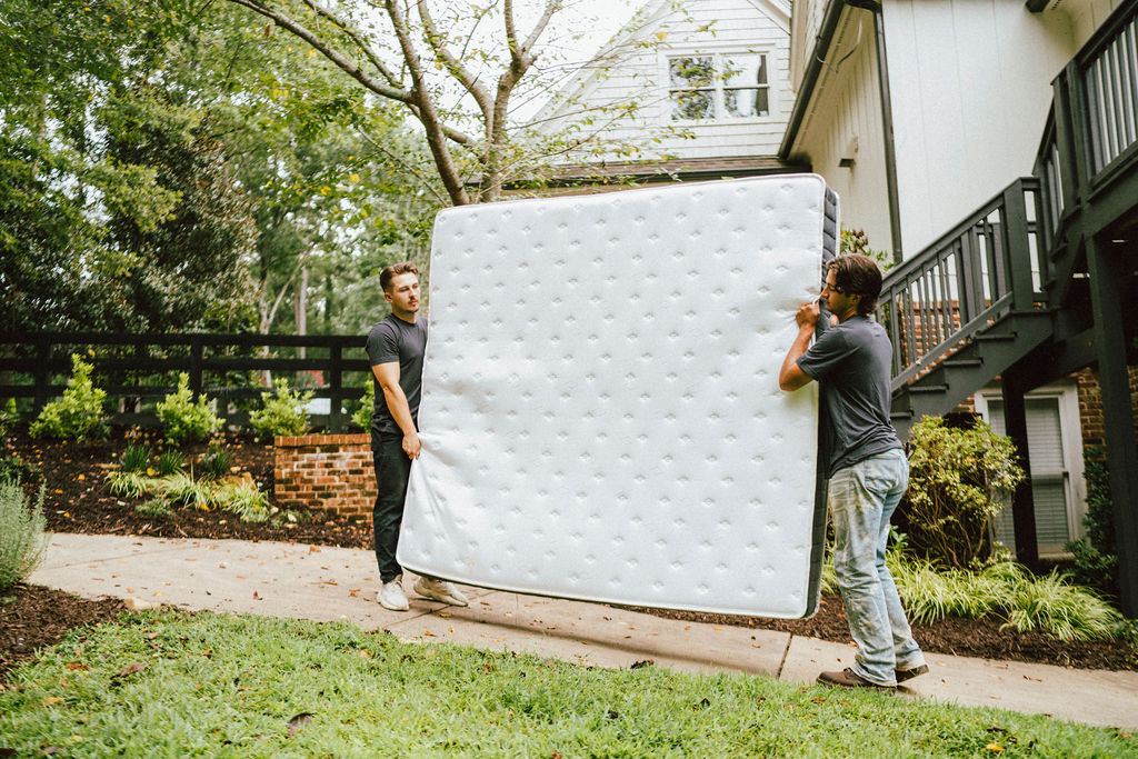 Two Loaders carrying an old mattress across a front yard during a curbside pickup