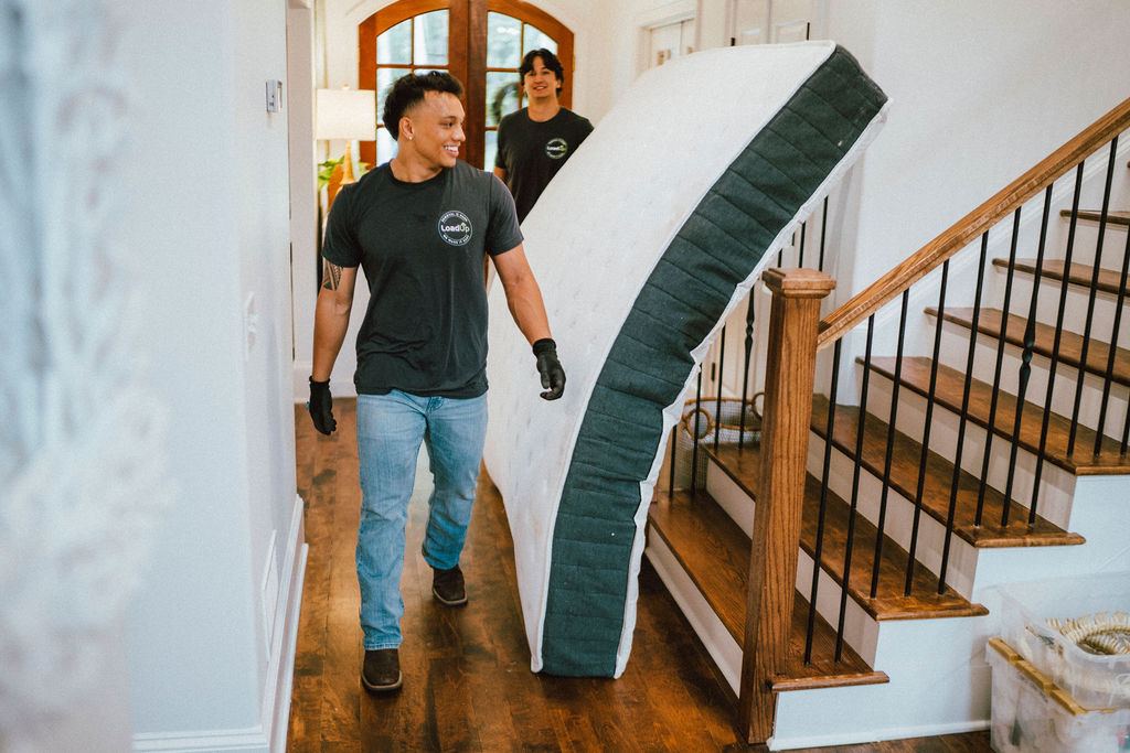A smiling Loader in a LoadUp shirt carrying a mattress through a home hallway